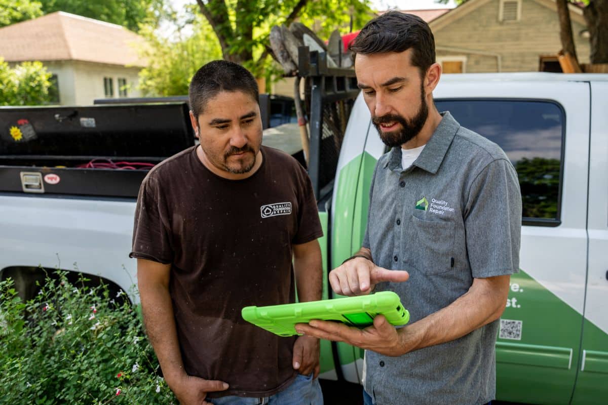 Quality Foundation Repair Austin team members conducting an on-site consultation with a tablet beside a branded service vehicle.