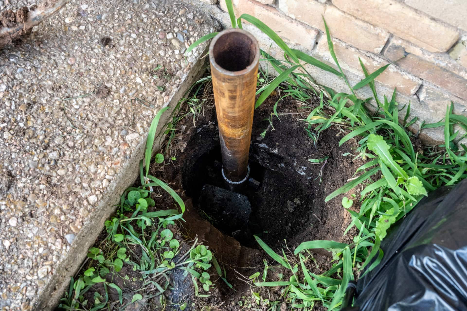 Quality Foundation Repair Austin installing a steel push pier in an excavation beside a brick foundation.