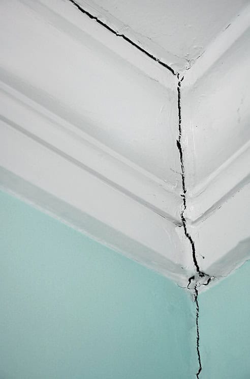 Quality Foundation Repair Austin inspecting a significant crack where a wall meets the ceiling.