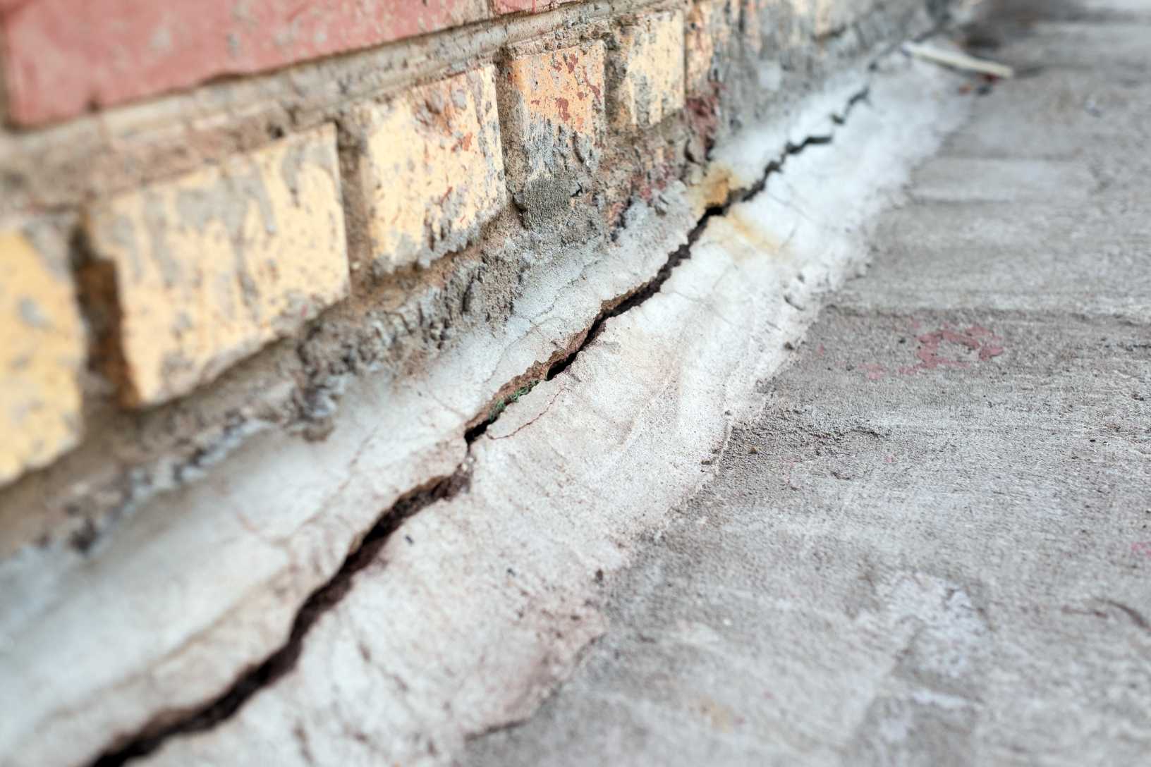 Quality Foundation Repair Austin inspecting a deep foundation crack at the base of a brick wall.