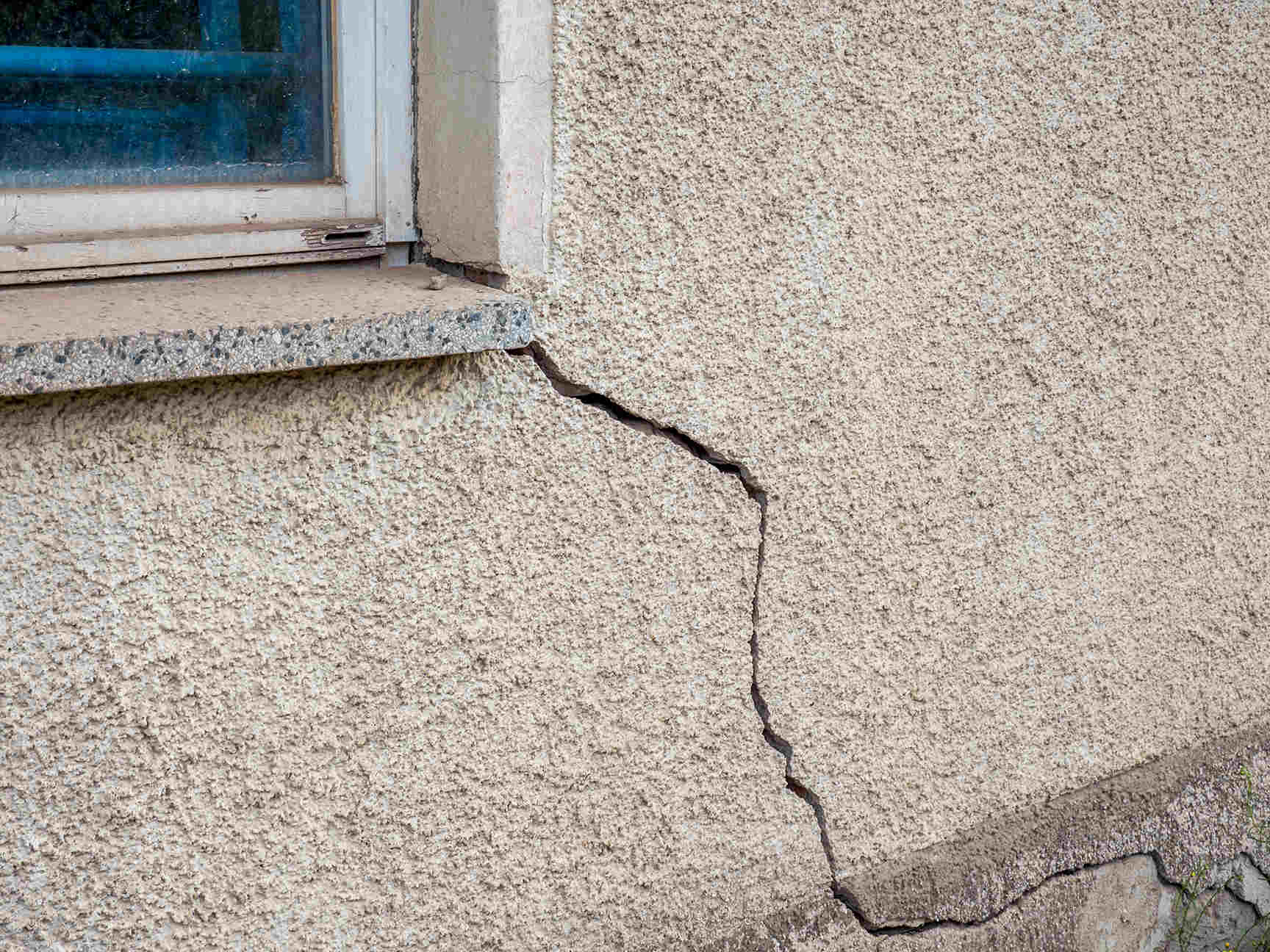 Quality Foundation Repair Austin inspecting a diagonal crack in a stucco exterior wall.