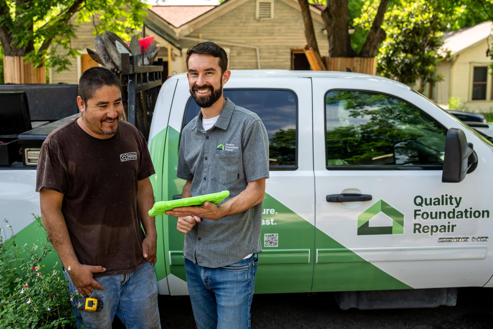 Quality Foundation Repair Austin team members discussing plans with a tablet in front of a branded company truck.