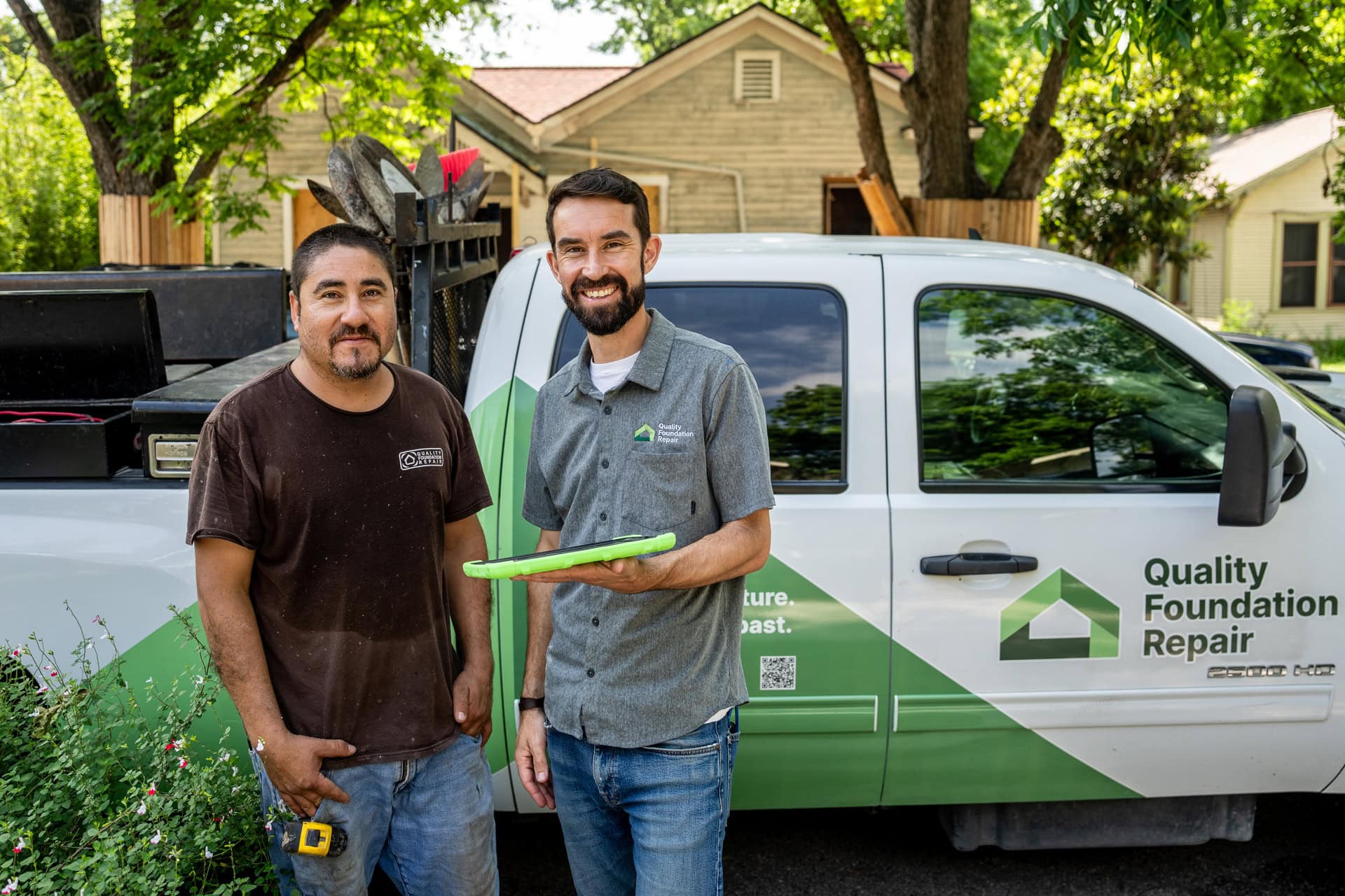 Quality Foundation Repair Austin team members standing by a branded company truck with a tablet.