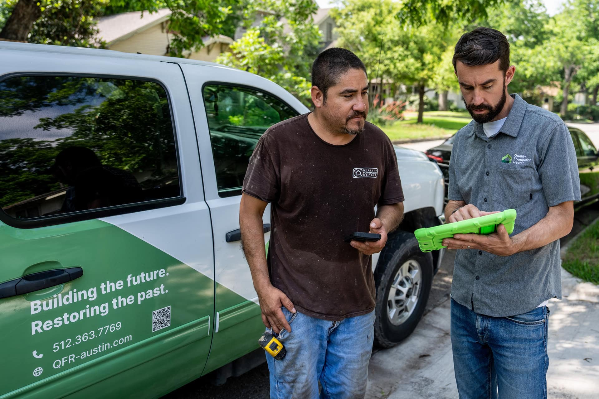 Quality Foundation Repair Austin team members conducting an on-site consultation, reviewing details on a tablet next to a branded company truck.