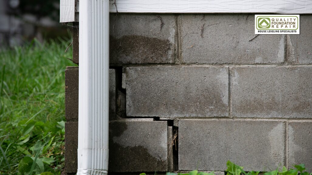 Quality Foundation Repair Austin inspecting stair-step cracks in a concrete block foundation with water damage near a downspout.