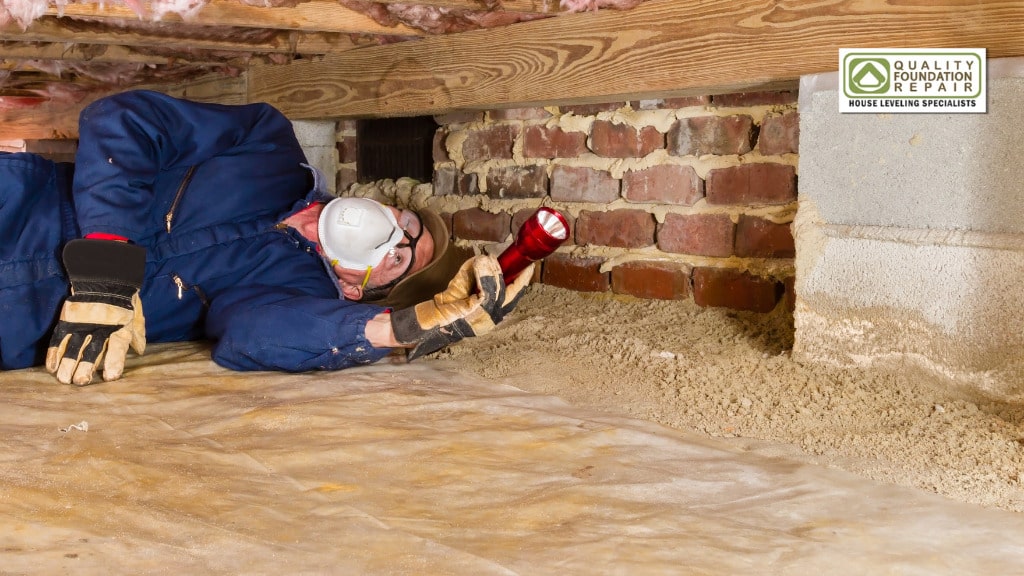 Quality Foundation Repair Austin technician inspecting a brick pier by torchlight in a crawl space.
