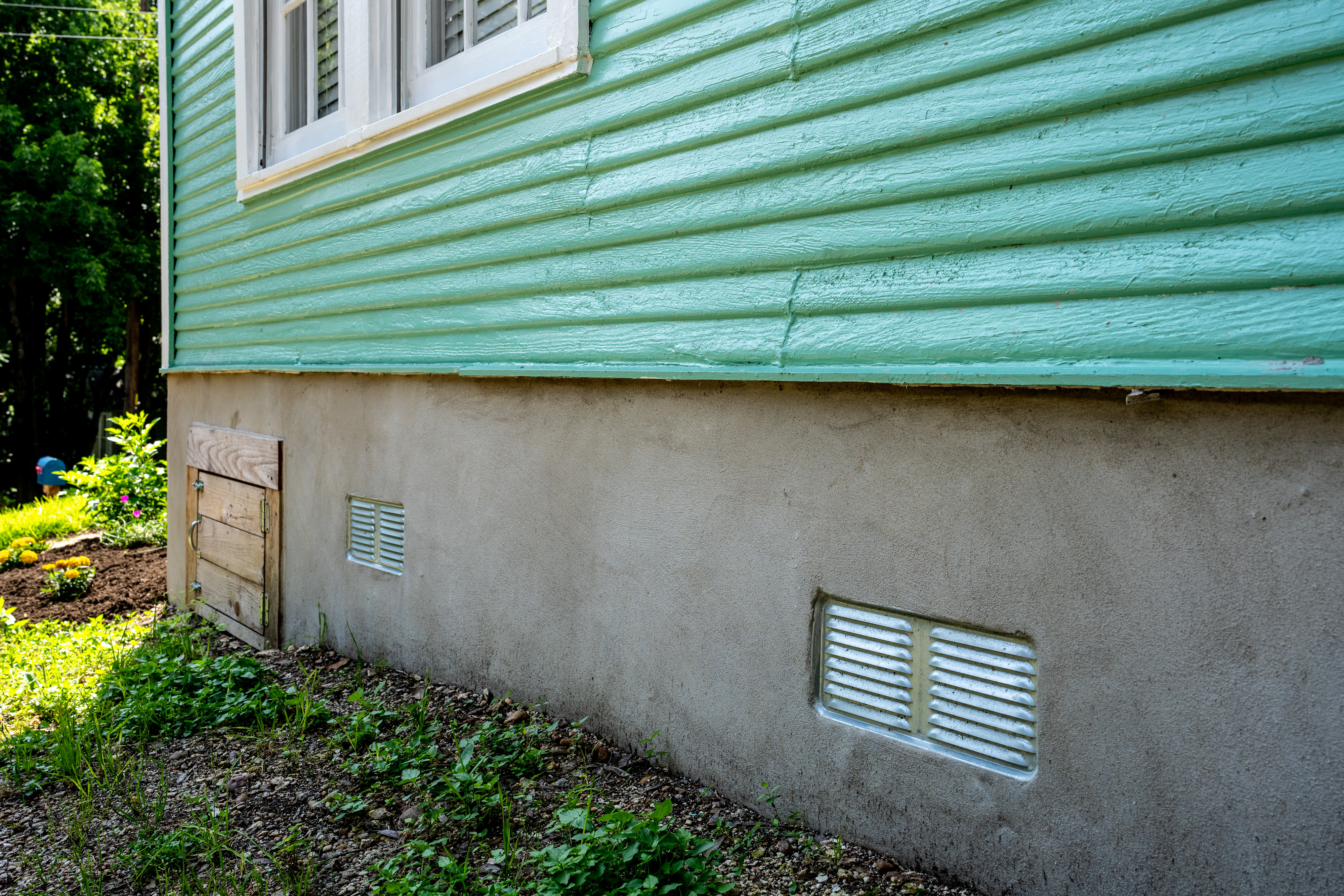 Quality Foundation Repair Austin inspecting the exterior crawl space access well and foundation vent covers of a residential home.