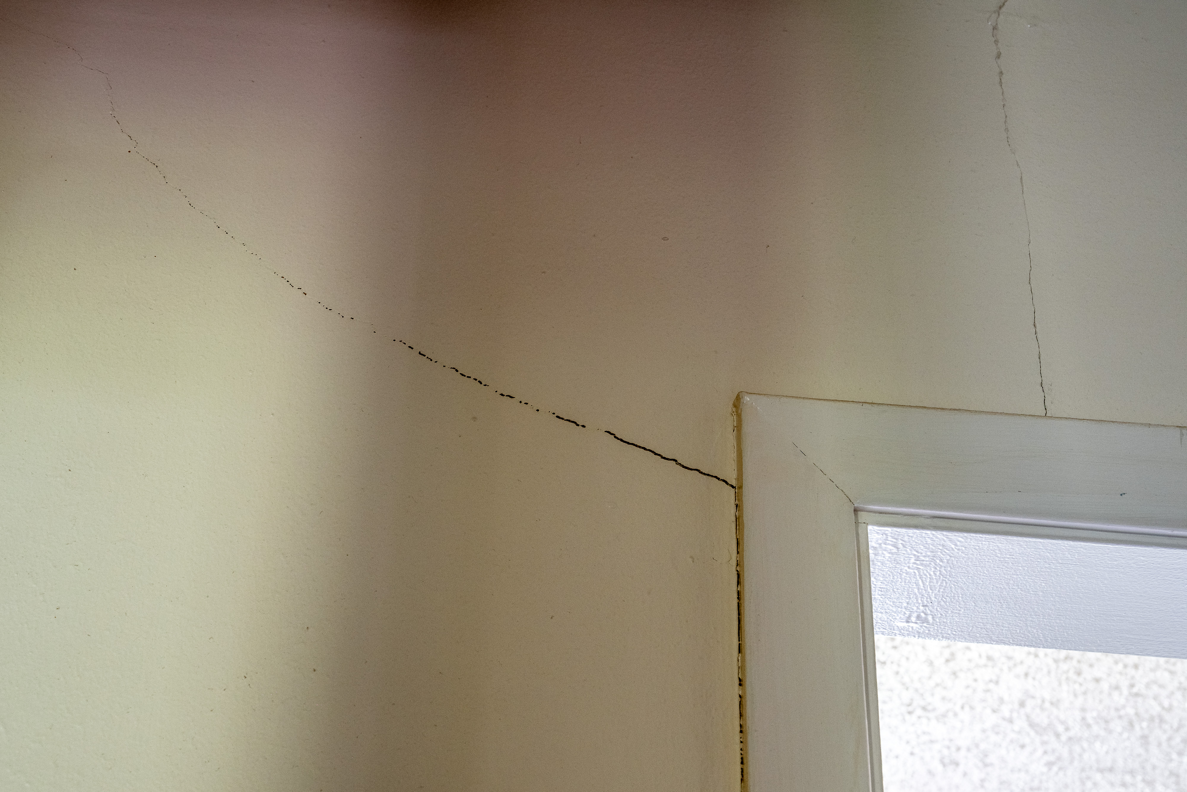 Quality Foundation Repair Austin inspecting diagonal cracks in drywall near a window frame, indicating foundation shifting.