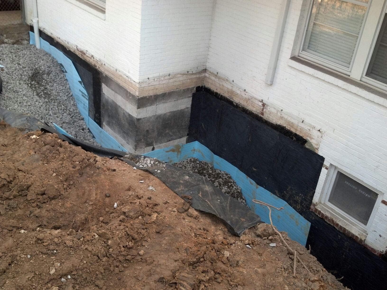 Installing an exterior waterproofing membrane and drainage around a foundation.
