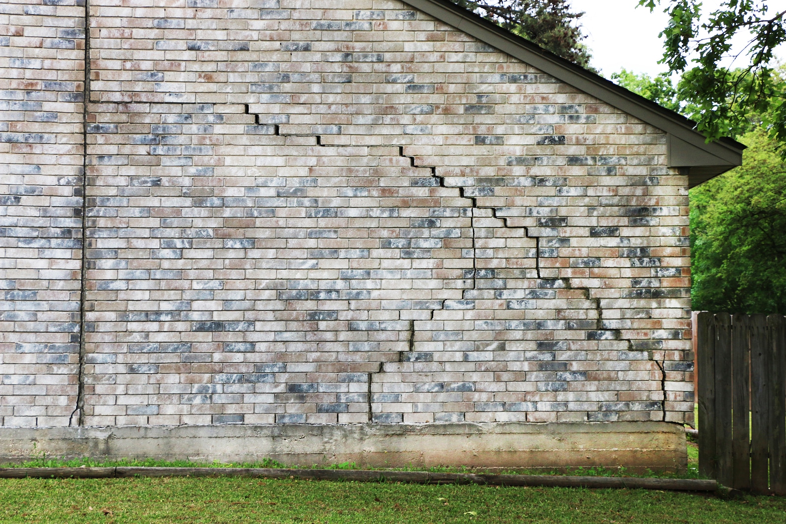 Inspecting a stair-step foundation crack on a brick exterior wall.