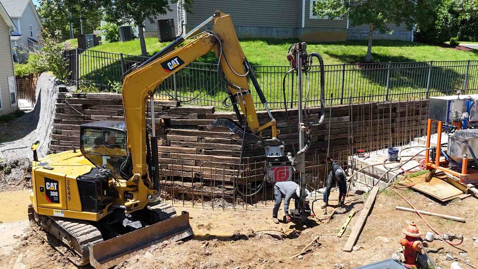A commercial crew performing foundation and retaining wall repair with heavy equipment.