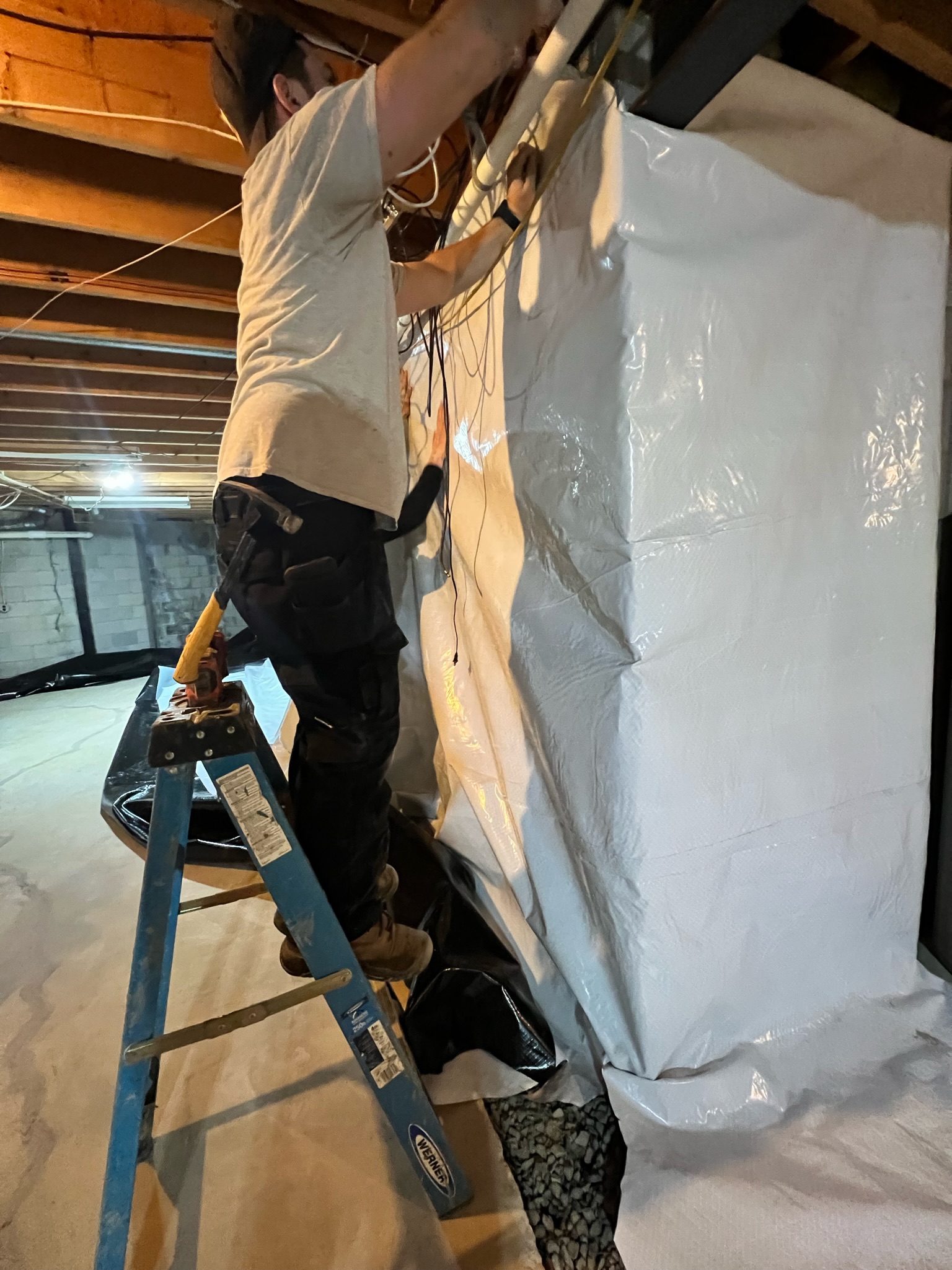 Oriole technician fastening vapor barrier along the top of a basement wall