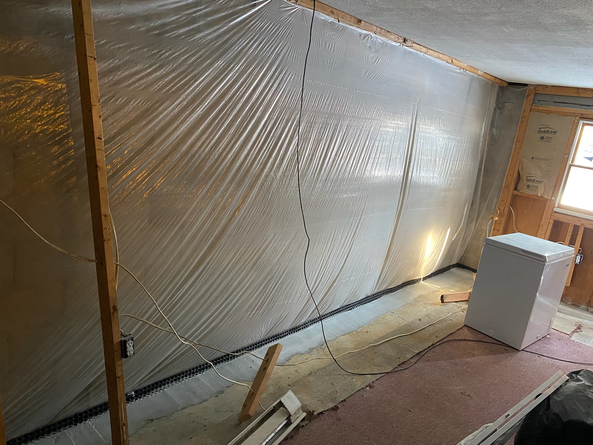 Sealed vapor barrier covering a basement wall from floor to sill plate