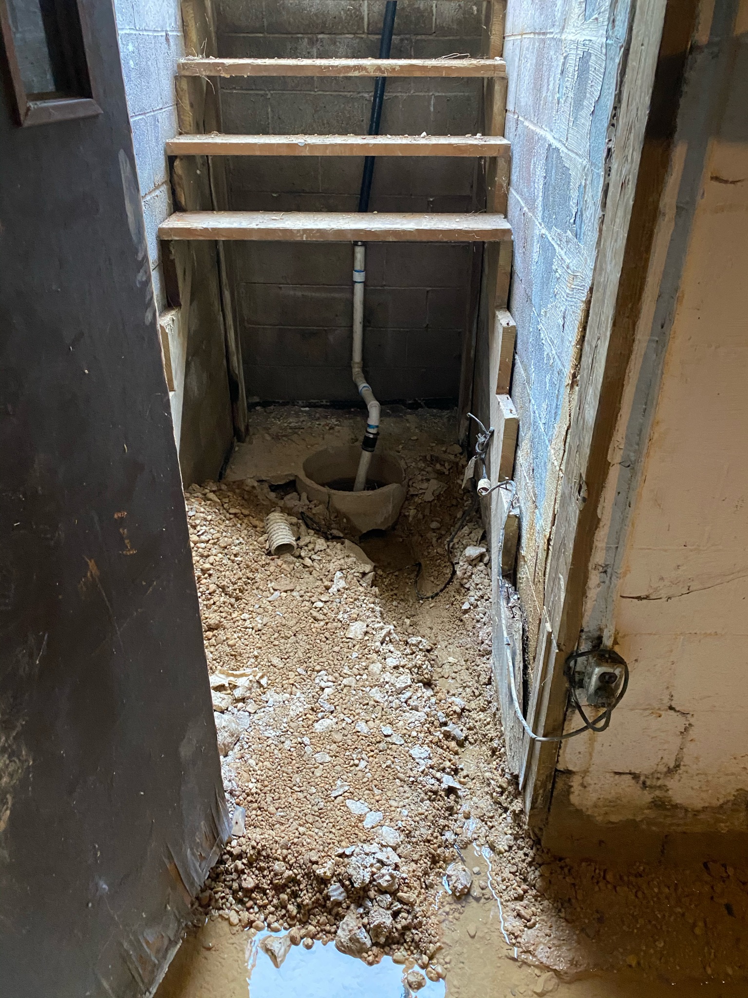 Flooded basement with standing water around an undersized sump pump pit in Maryland