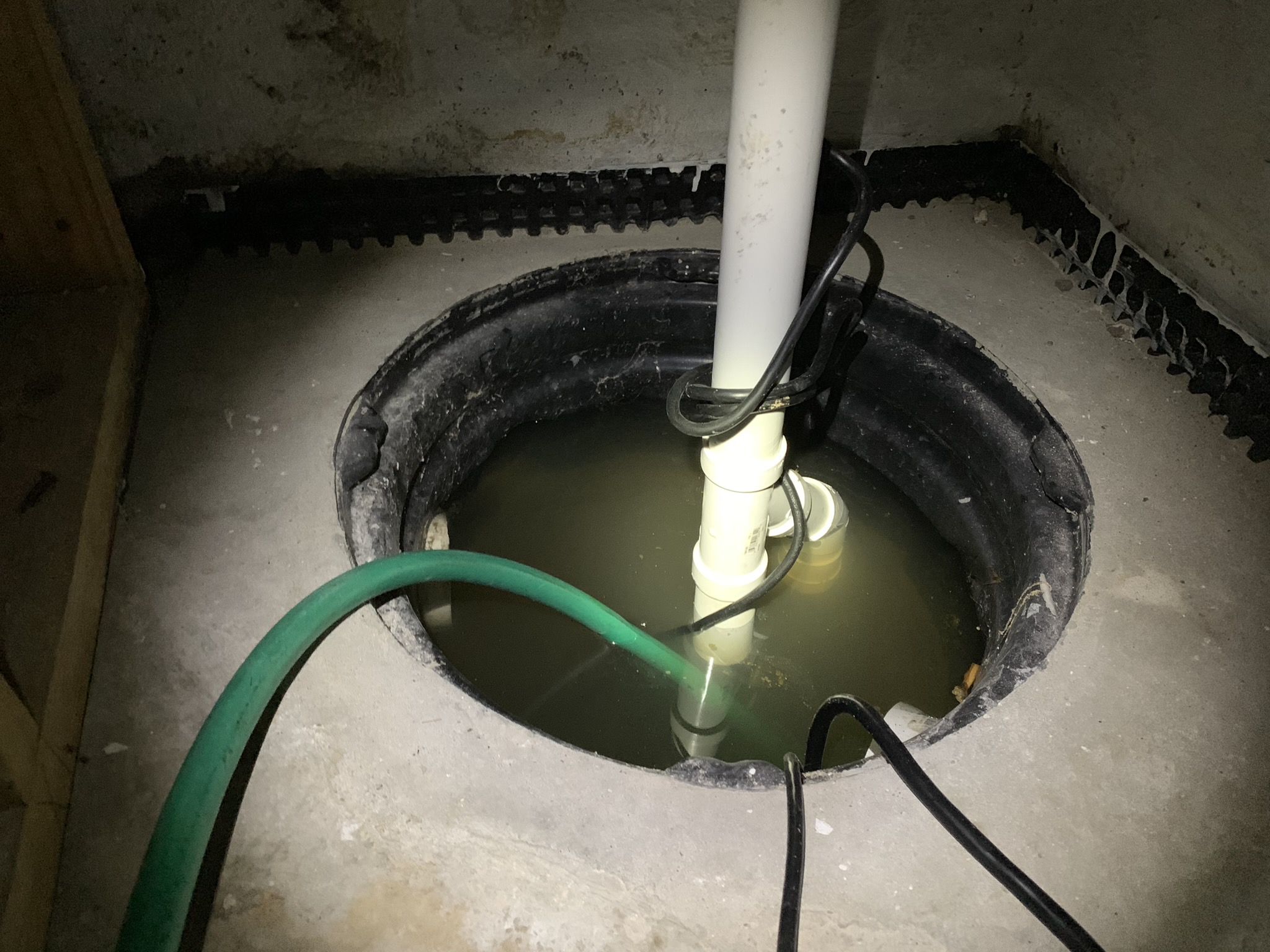 Flooded sump pump pit with drainage matting in a Maryland basement