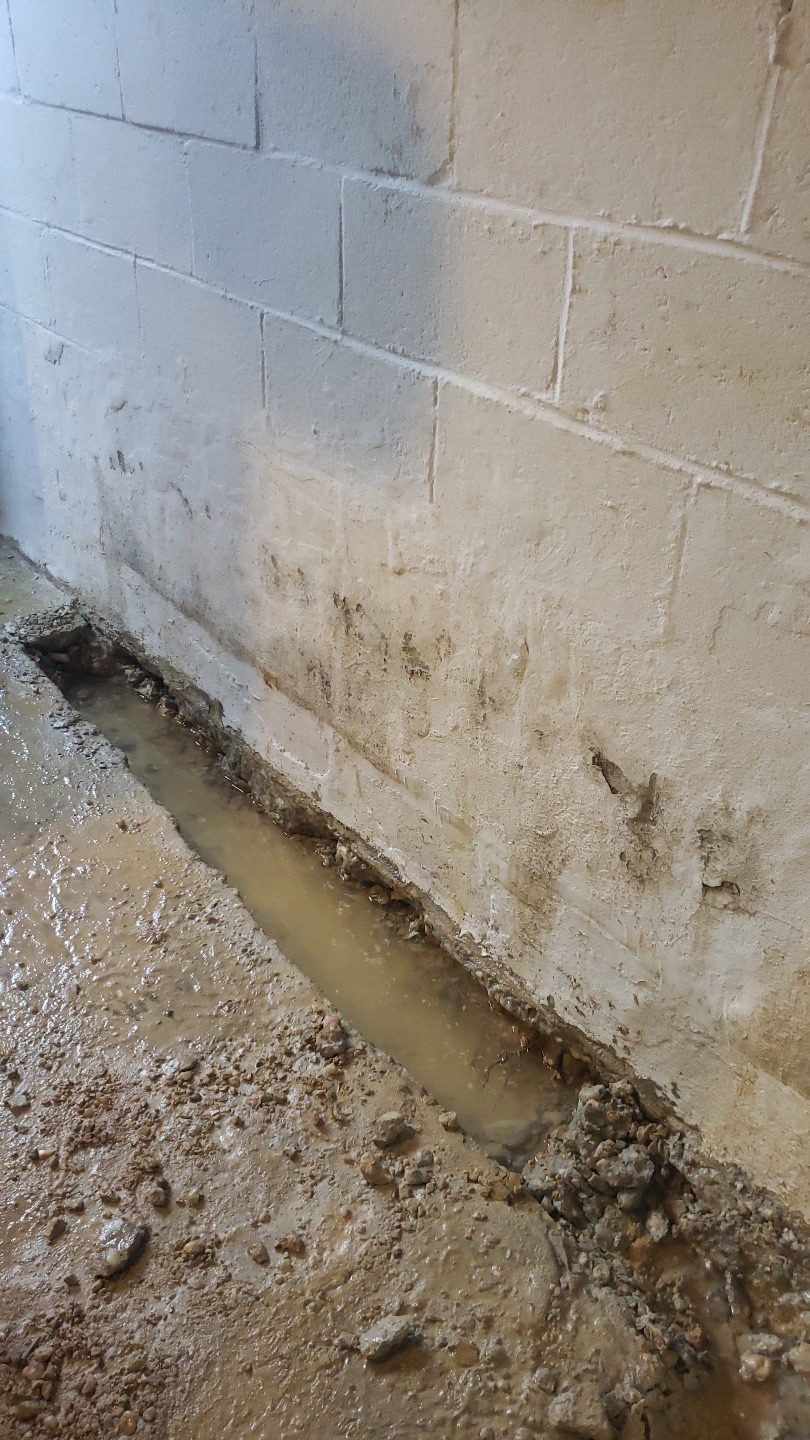 Flooded Maryland basement with standing water and a drainage trench