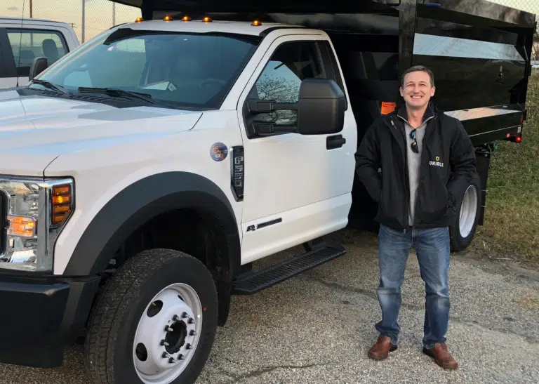 Frank Pirog III smiling in an Oriole jacket in front of a company dump truck