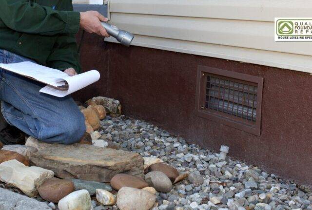 Quality Foundation Repair Austin technician inspecting a crawl space foundation vent with a flashlight and clipboard.
