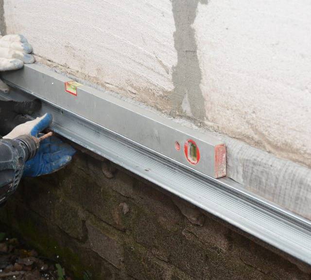 Quality Foundation Repair Austin technicians performing structural leveling and foundation repair using a level and drill.