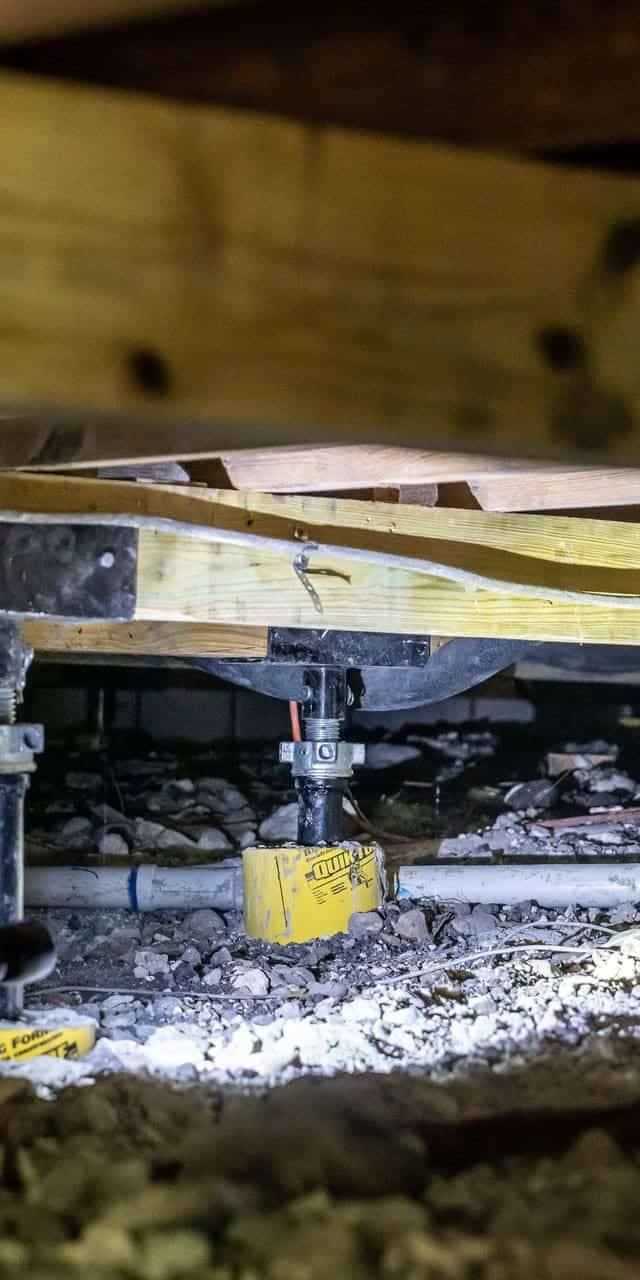 Quality Foundation Repair Austin technician inspecting and installing crawl space support jacks in a confined crawl space.