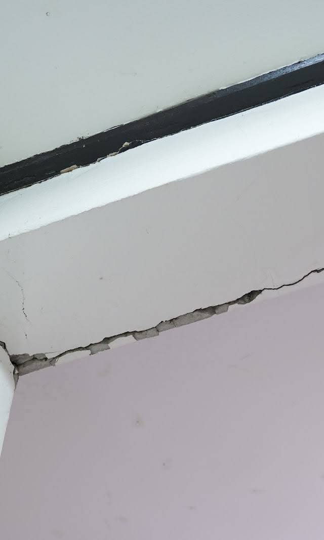 Quality Foundation Repair Austin inspecting a significant crack where an interior wall meets the ceiling, indicating structur