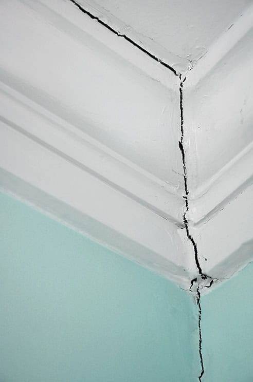 Quality Foundation Repair Austin inspecting a significant crack where a wall meets the ceiling, a sign of dangerous ceiling g