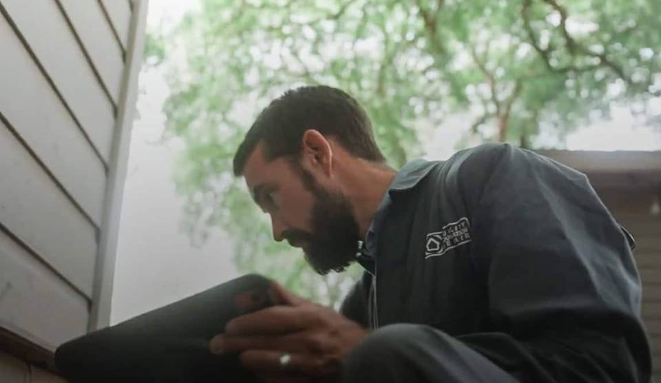 A Quality Foundation Repair Austin technician reviewing inspection notes on a tablet beside a home.