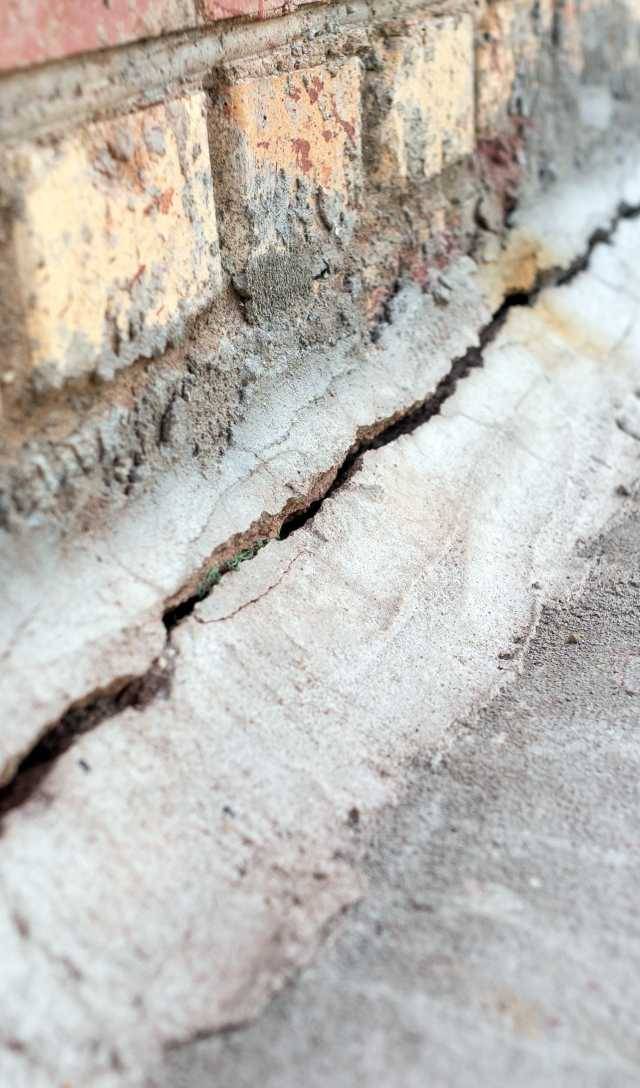 Quality Foundation Repair Austin inspecting a deep foundation crack at the base of a brick wall.