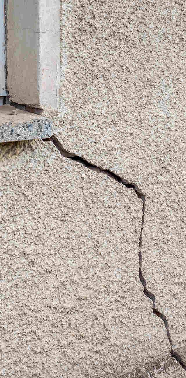 Quality Foundation Repair Austin inspecting a diagonal crack in a stucco exterior wall, indicating potential foundation movem